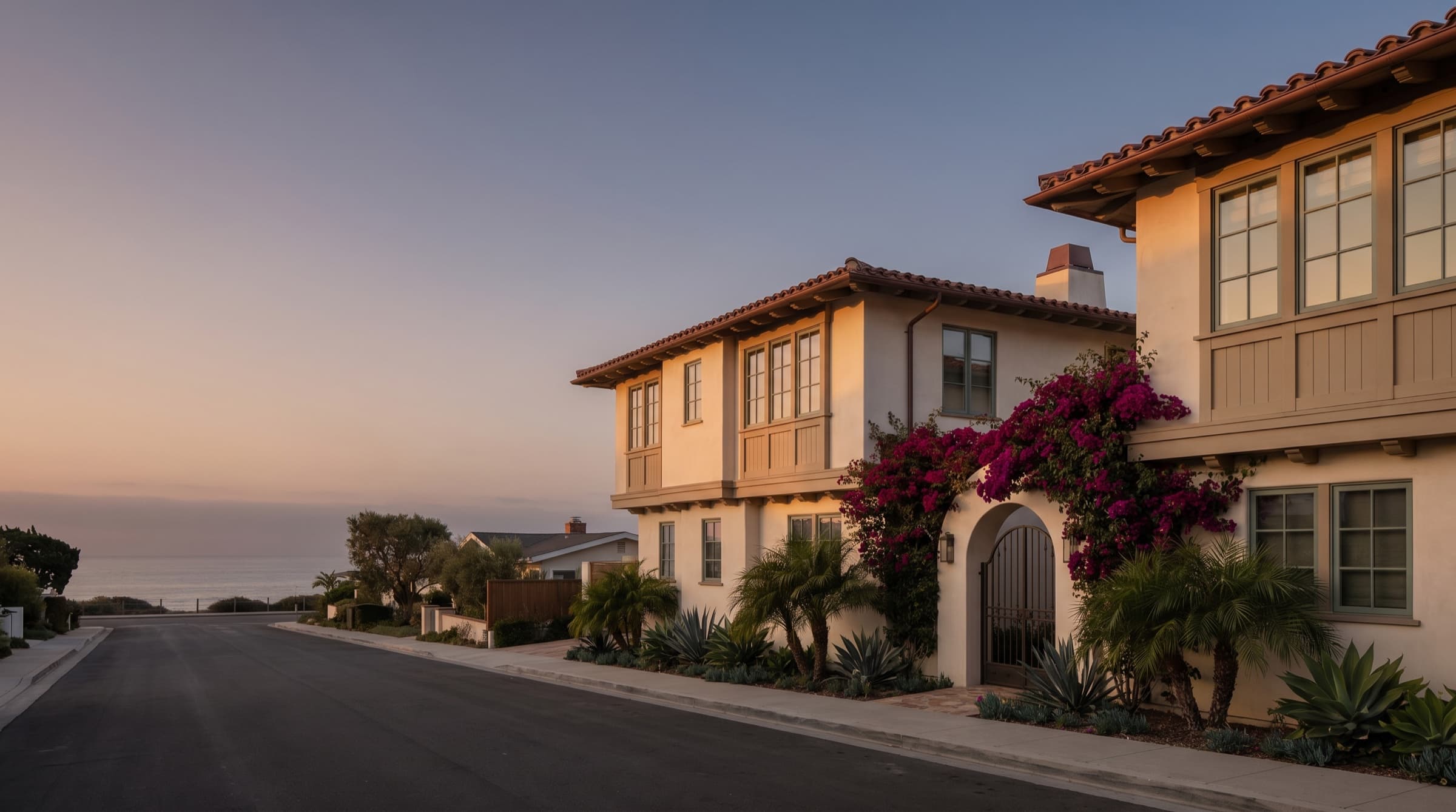 Wide cinematic view of a coastal California Spanish-stucco fourplex at dusk with the Pacific horizon visible, illustrative of the asset class